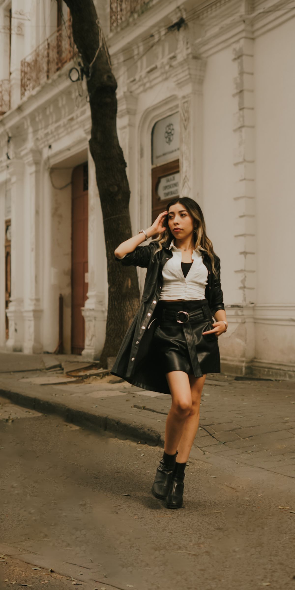 A stylish young woman in black leather skirt and jacket walking on a city street.