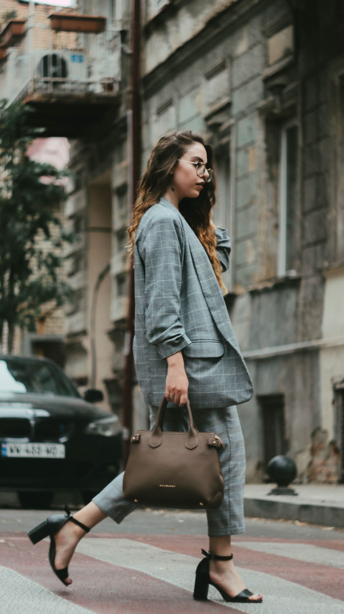 Trendy woman in plaid outfit walking on an urban street holding a handbag.
