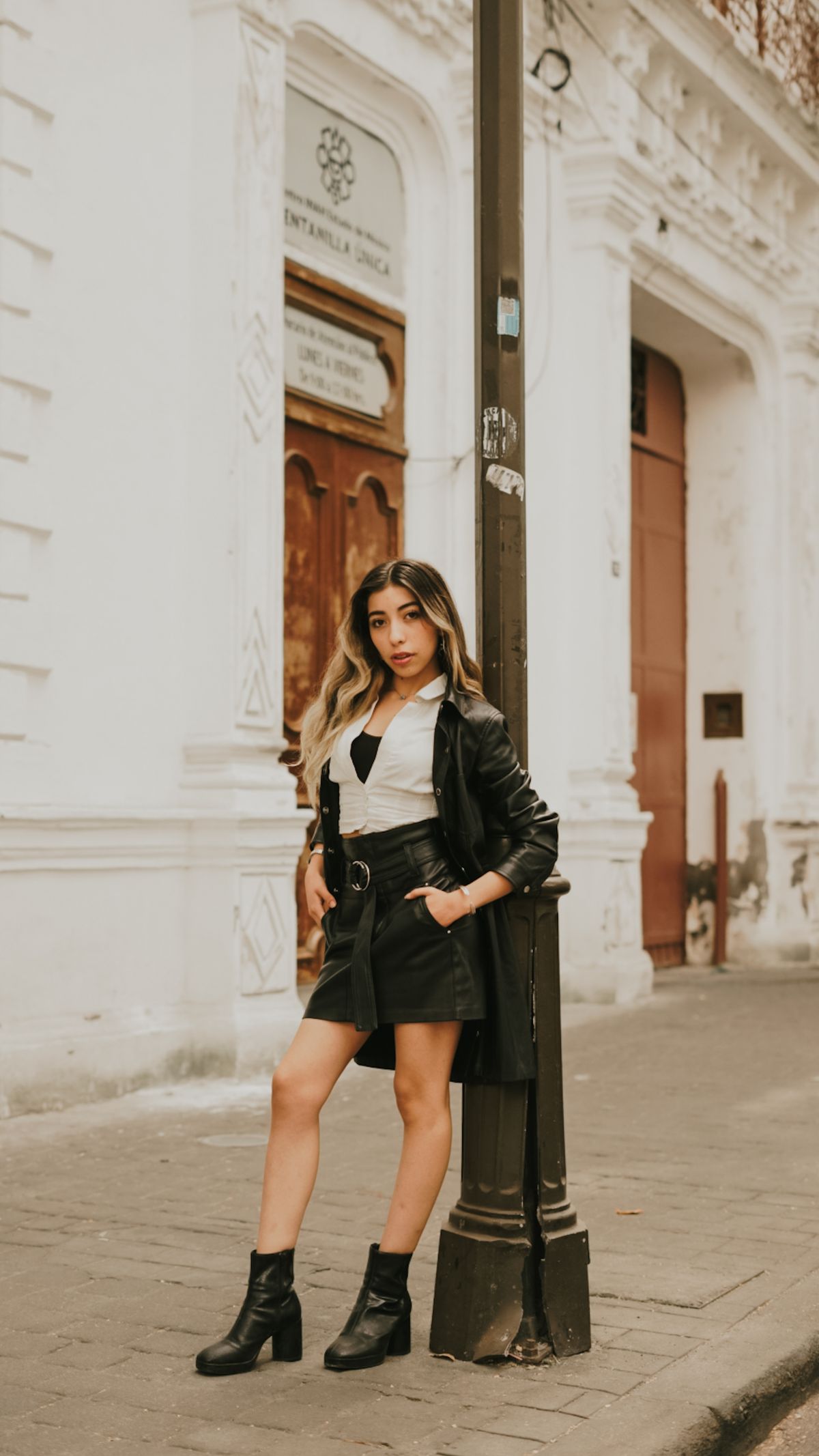 Fashionable woman in urban setting during daytime, posing confidently by a lamppost.