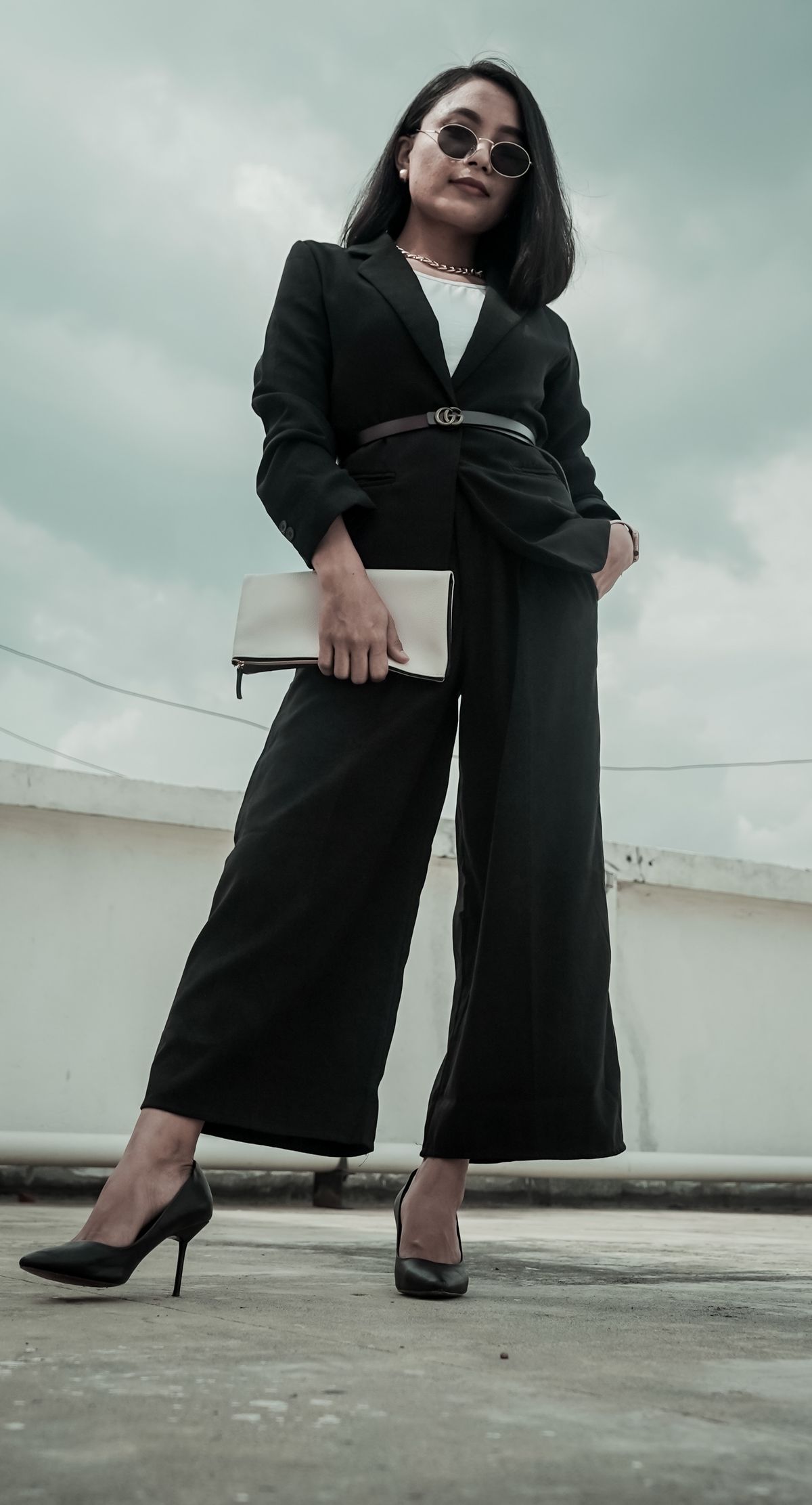 Ground level of young ethnic woman in trendy clothes and sunglasses standing with hand in pocket in overcast weather
